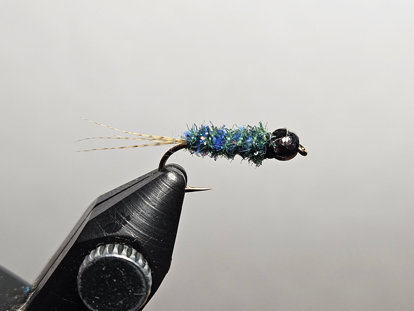 A blue and green iridescent variation of the Maple syrup fly pattern, a New England pond classic invented by Maine angler and tyer Alvin Theriault, tied by New England Fly Company